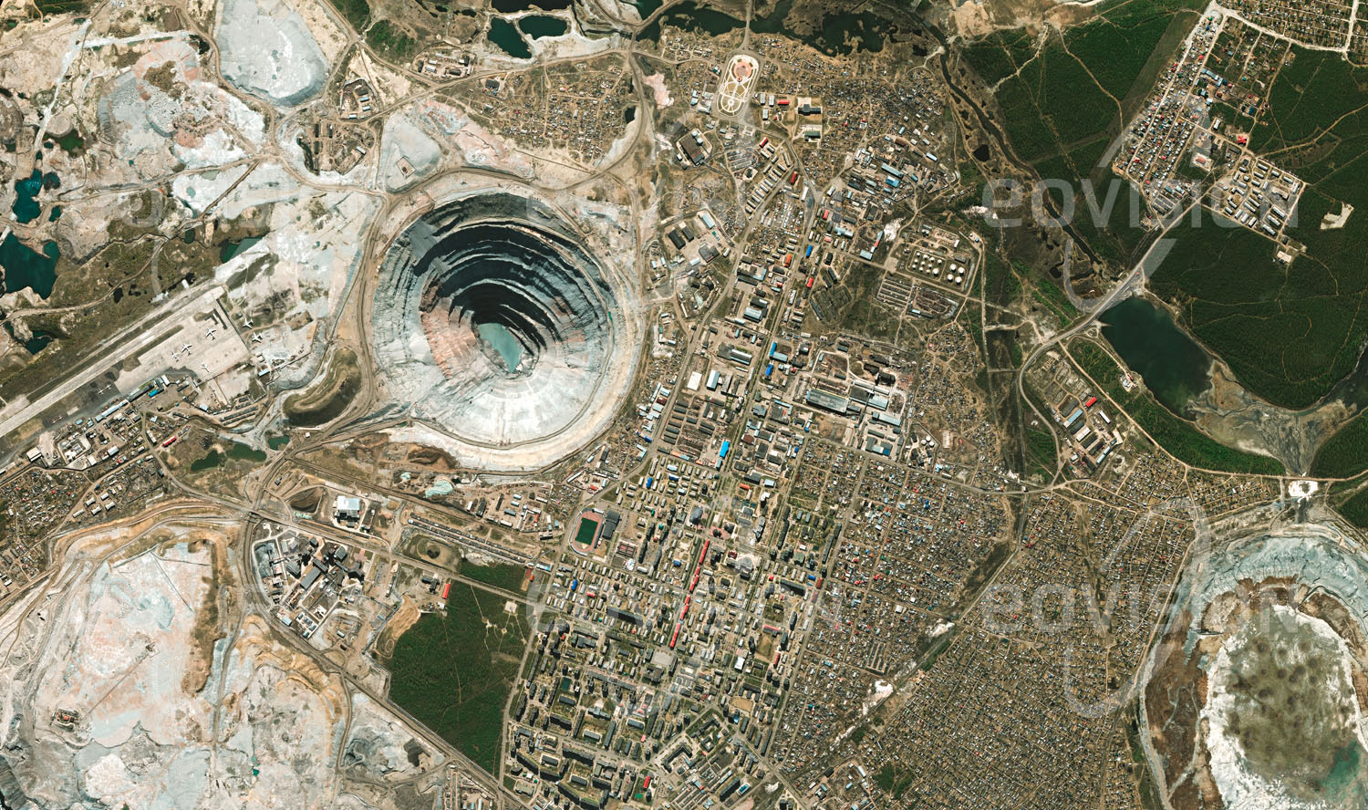 Das Satellitenbild 'MIRNY, Russland' ist dem Bildband "Cities - Brennpunkte der Menschheit" entnommen. Mirny wurde im Jahr 1955 nach dem Fund der ersten sibirischen Diamantvorkommen gegründet, um diese auszubeuten. Die Bergbaustadt im Permafrostgebiet des russischen Jakutien ist unmittelbar um die Diamantmine Mir angeordnet, mit 525 Meter Tiefe und 1,2 Kilometern Durchmesser eine der weltweit größten Minen im Tagebau. Nachdem die Diamantförderung stark zurückgegangen war, wurde die Mine ab dem Jahr 2001 schrittweise geschlossen.