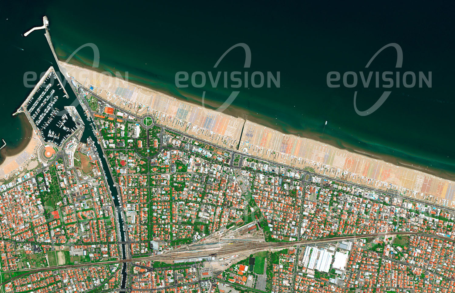 Das Satellitenbild 'RIMINI, Italien' ist dem Bildband "Europa - Kontinent der Vielfalt" entnommen. Militärisch exakt angeordnet und durch ihre Farbe gut unterscheidbar bedecken Sonnenschirme die Adriaküste bei Rimini. Gemeinsam mit dem mediterranen Klima und der guten Erreichbarkeit stellt der 15 Kilometer lange Sandstrand die Grundlage für den Sommertourismus in der Region dar — schon 1843 entstand hier die erste Badeanlage an der Adria. n