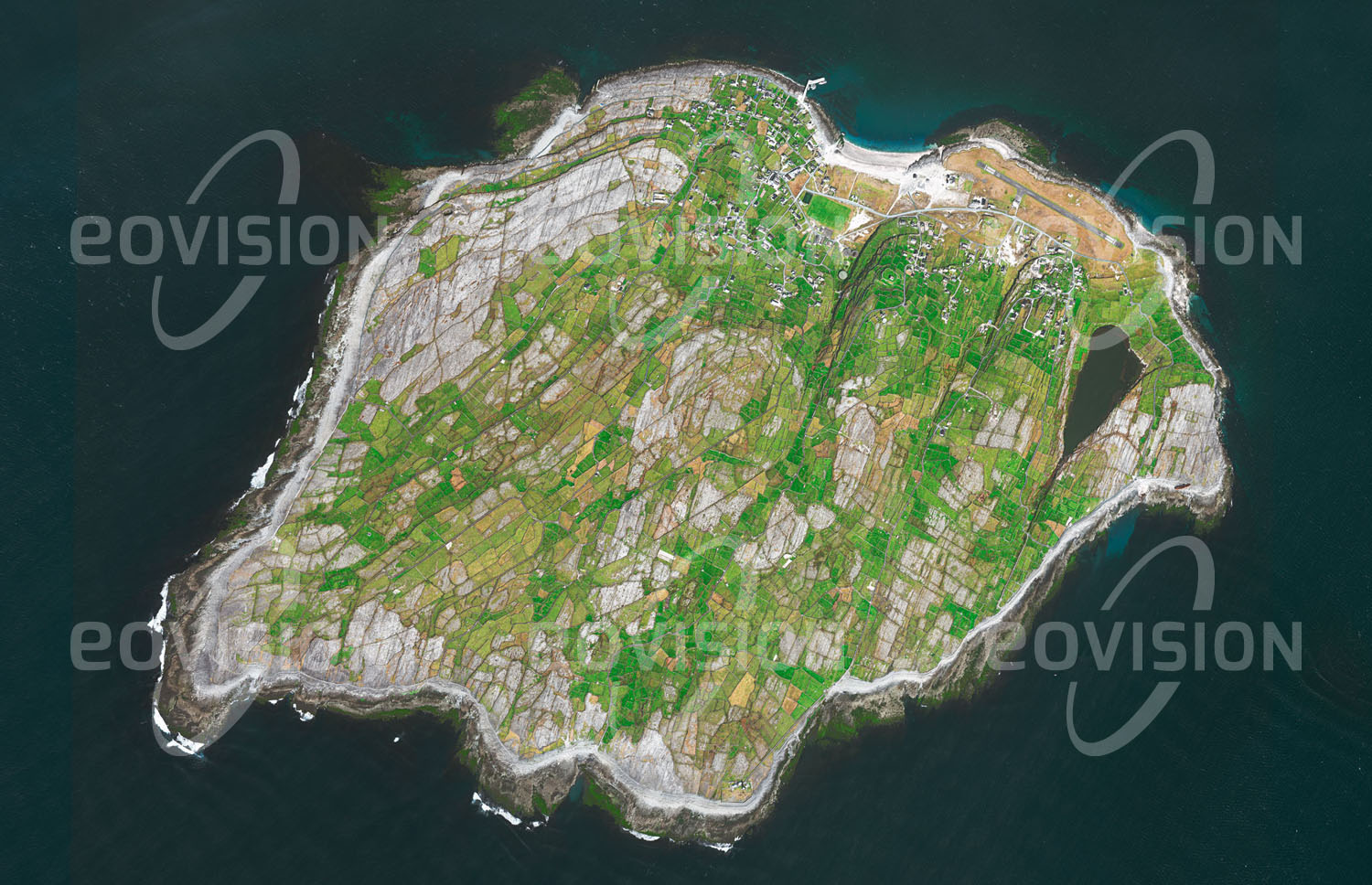 Das Satellitenbild 'INISHEER, Irland' ist dem Bildband "Europa - Kontinent der Vielfalt" entnommen. Die kleine Felseninsel Inisheer oder Inis Oírr liegt als Teil der Aran Islands vor der Westküste Irlands. Während der Eiszeiten wurde der Kalkfelsen durch Gletscher abgeschliffen, zahlreiche vom Wasser ausgewaschene Spalten durchziehen die Karstlandschaft. Da sich Erde auf diesem Untergrund nur schwer hält, ist die ganze Insel von Steinmauern überzogen, die den Humus stabilisieren sollen. Heute wird allerdings die Landwirtschaft auf Inisheer immer mehr vom Tourismus abgelöst.n