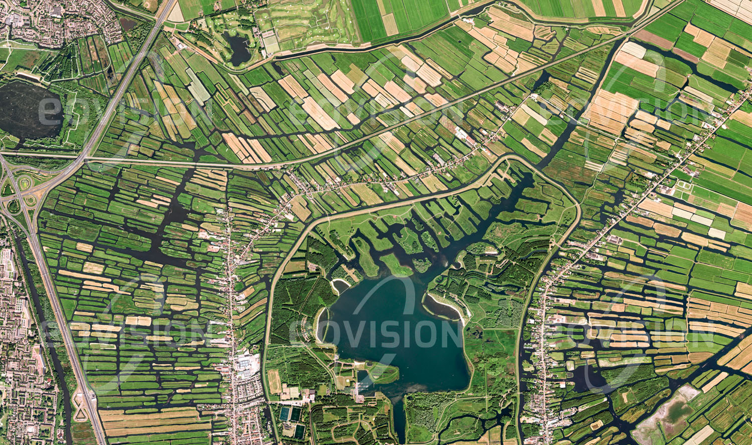 Das Satellitenbild 'OOSTZAAN, Niederlande' ist dem Bildband "Human Footprint - Satellitenbilder dokumentieren menschliches Handeln" entnommen. Durch Deichbau und Entwässerung im Watt entstand unmittelbar nördlich an Amsterdam anschließend eine charakteristische Polder-landschaft, ein Muster aus Kanälen und flachen Marschwiesen. Für die Sicherheit des einige Meter unterhalb des Meeresspiegel gelegenen Gebiets sind die umliegenden Deiche ebenso wichtig wie die Pumpen, die früher durch Windräder angetrieben wurden.