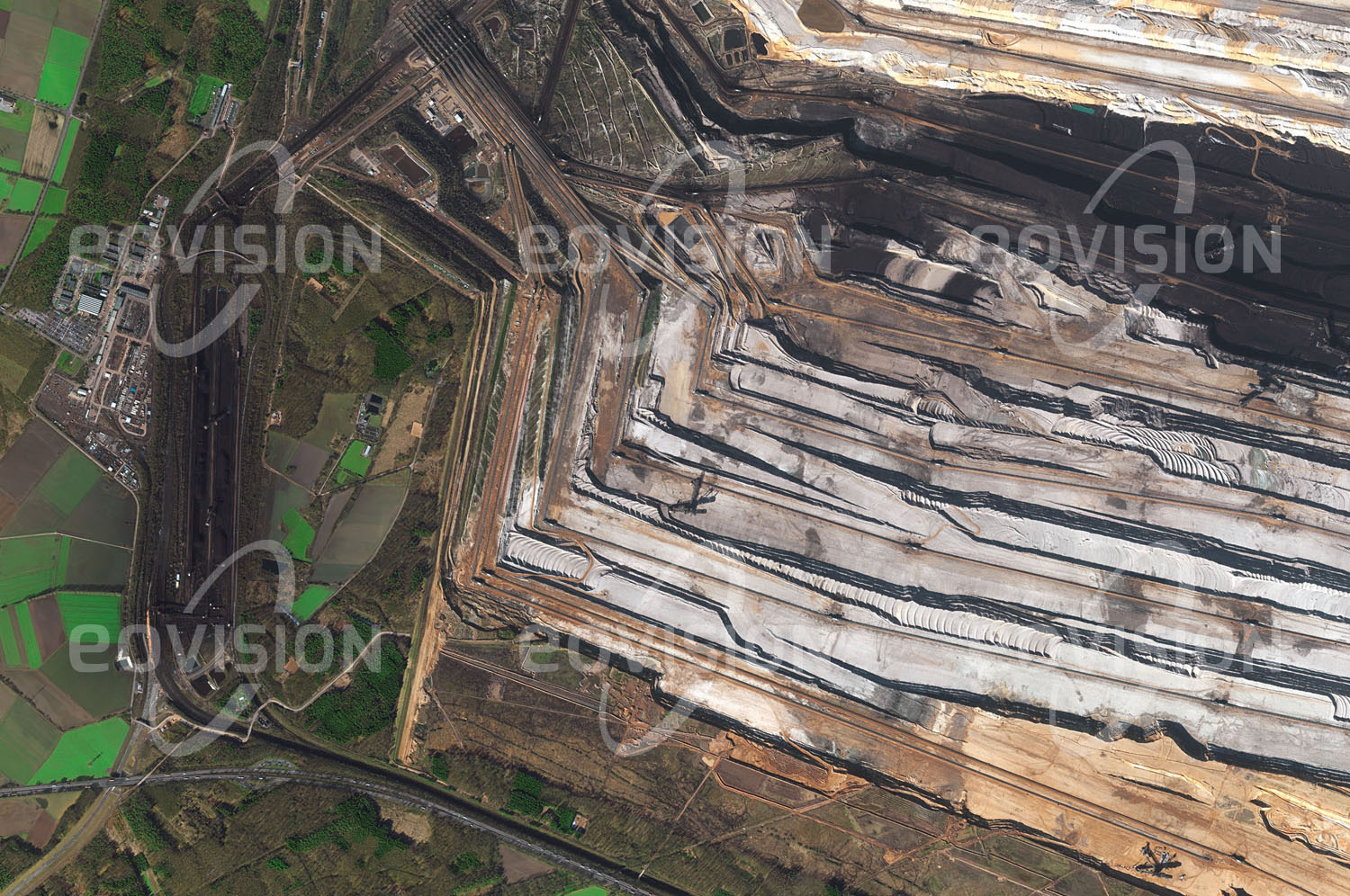 Das Satellitenbild 'HAMBACH, Deutschland' ist dem Bildband "New Human Footprint - Unsere Welt im Umbruch" entnommen. Obwohl Braunkohle einen vergleichsweise geringen Energiegehalt besitzt und auch we­gen ihrer hohen Schwefelkonzentration die Umwelt stärker belastet als andere Energie­träger, wird sie vor allem in Deutschland und Polen noch stark genutzt. In ausgedehnten Revieren wie Hambach frisst sich der Tage­bau durch die Landschaft, im Weg stehende Ortschaften müssen umgesiedelt werden. Die nicht mehr genutzten Bereiche werden renaturiert. In Hambach werden jedes Jahr 40 Millionen Tonnen Braunkohle für die Kraftwerke um Köln gefördert. Geplant ist, die Förderung bis 2040 fortzusetzen.