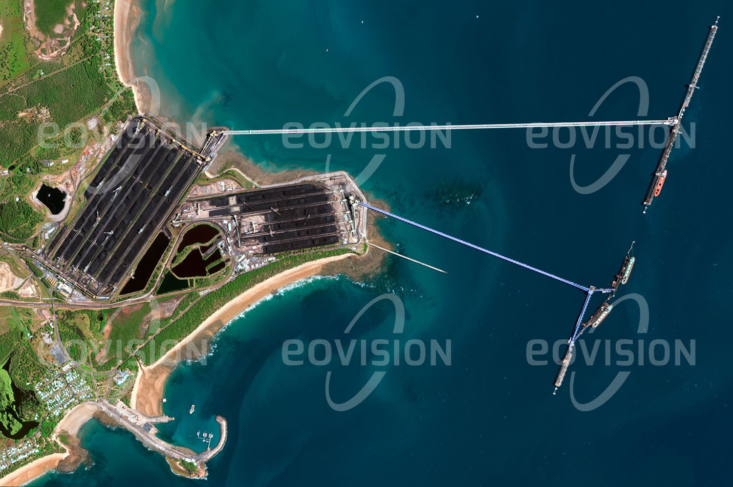 Das Satellitenbild 'HAY POINT, Australien' ist dem Bildband "New Human Footprint - Unsere Welt im Umbruch" entnommen. Vor der Küste Queenslands im Nordosten Australiens liegt einer der größten Kohle­häfen der Welt. An zwei Terminals werden über lange Förderbänder Kohlefrachter beladen. Im Bild sind die Halden der Kohlen unübersehbar, die von den Kohleminen von Queensland mit der Bahn hierher zum Ver­schiffen gebracht werden. Zuletzt wurden an diesen Terminals mehr als 120 Millionen Tonnen Kohle pro Jahr verladen. Wegen der Nähe des Great Barrier Reefs, eines marinen Schutzgebiets von Weltrang, gab es vor wenigen Jahren heftige Proteste gegen die Erweiterung des Terminals.