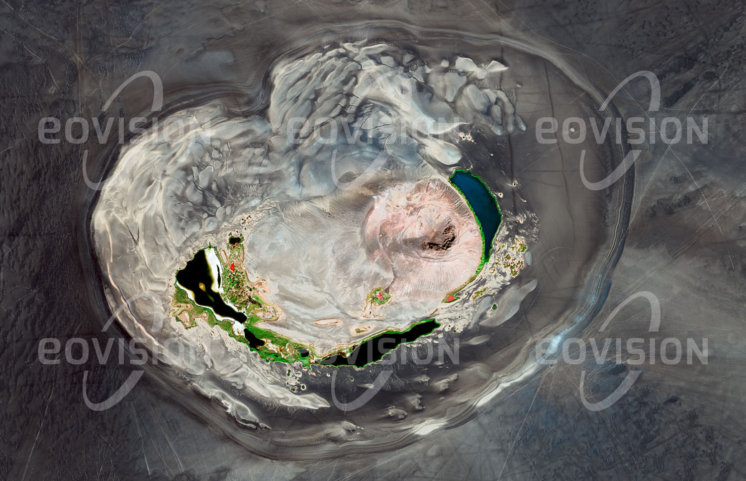 Das Satellitenbild 'WAW AN-NAMUS, Libyen' ist dem Bildband "Wüsten - Lebensraum der Extreme" entnommen. Waw an-Namus ist ein erloschener Vulkan im Süden Libyens. Alter und Ursprung des Vulkanismus in dieser Region im Herzen der Sahara sind nicht sicher bekannt. Die helle Caldera mit mehr als vier Kilometer Durchmesser ist umgeben von dunklem Eruptionsmaterial (Tephra). Innerhalb der Caldera befindet sich ein Vulkankegel aus hellem Auswurfgestein. Waw an-Namus bedeutet Moskito-Oase, weil um die Seen am Grund der Caldera zahlreiche Mücken leben. Die Seen erscheinen in unterschiedlichen Farben, die vom Salz- und Algengehalt des Wassers abhängen.